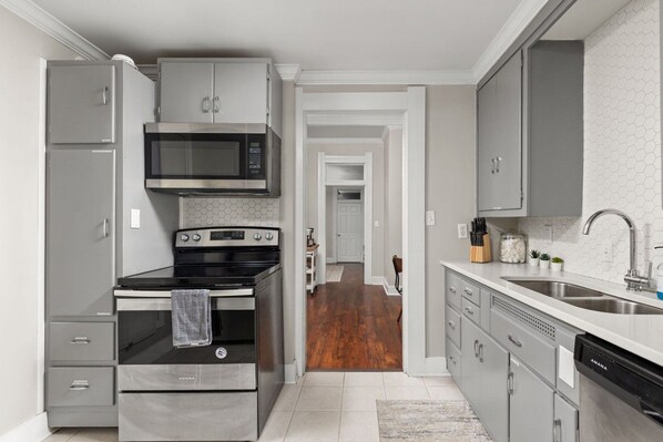 A modern kitchen with stainless steel appliances, grey cabinetry, and a visible hallway leading to another room.