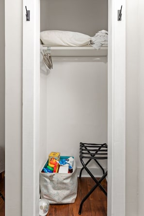 A small, white closet with a hanging rack and a storage bin containing colorful items.