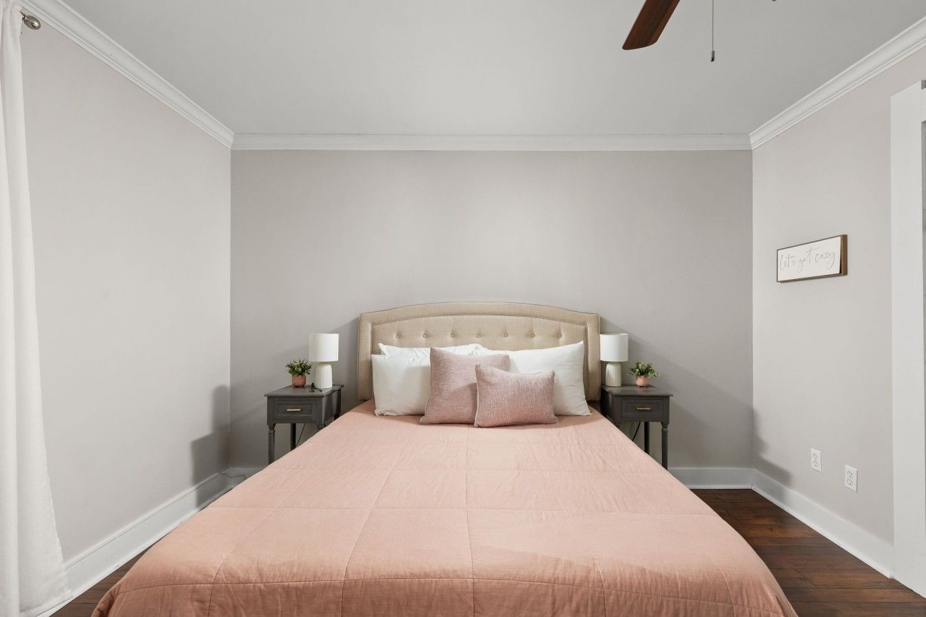 A bedroom with a large bed, two bedside tables with lamps, a ceiling fan, and a framed sign on the wall.