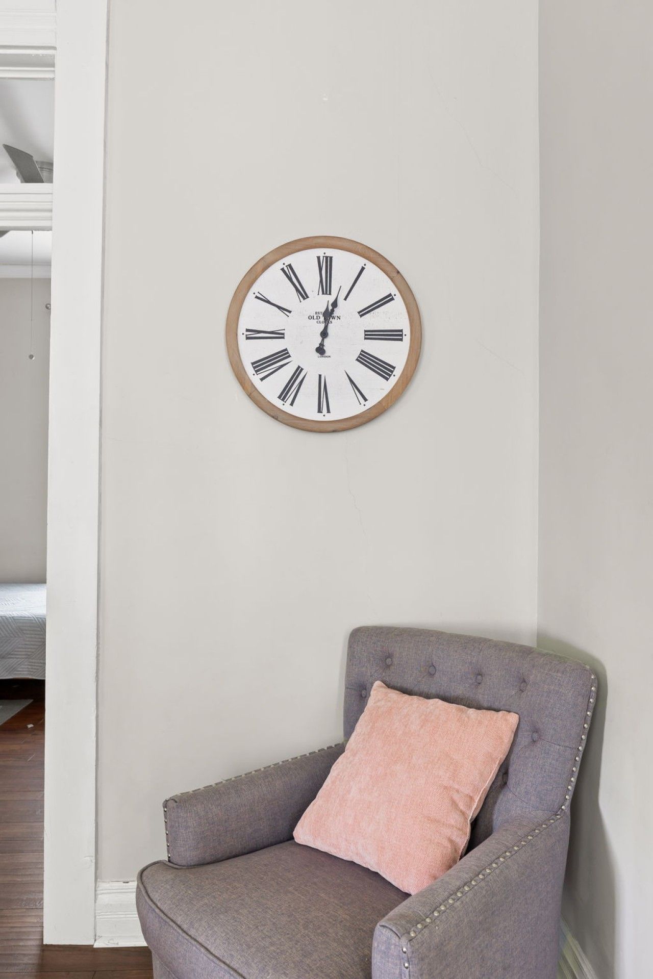 Une pièce comprenant un fauteuil à revêtement gris, une horloge murale à cadre en bois et un mur blanc.