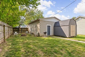 A backyard with a wooden fence, a shed, and a barbecue grill.