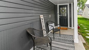 A house exterior with a dark gray siding, a black front door, and two wicker chairs outside.