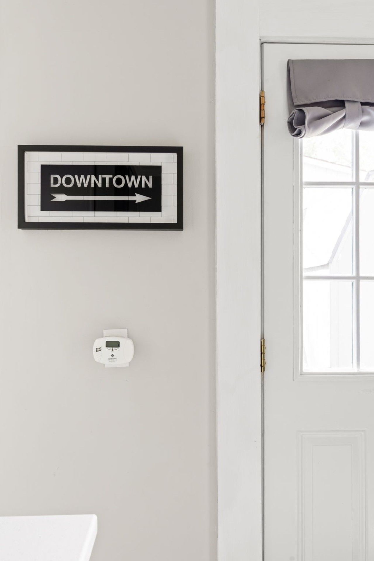 Une pancarte encadrée avec le mot « CENTRE-VILLE » et une flèche pointant vers la droite, un thermostat et une fenêtre avec un rideau.