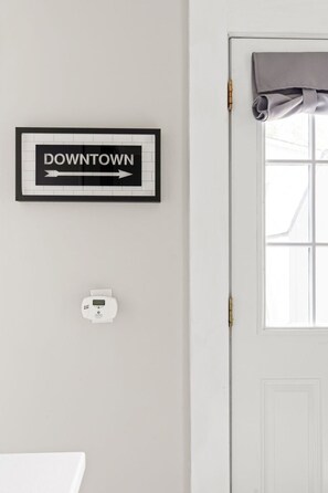 Une pancarte encadrée avec le mot « CENTRE-VILLE » et une flèche pointant vers la droite, un thermostat et une fenêtre avec un rideau.