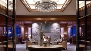 A lobby with a large round table, seating, a chandelier, and a stone wall.