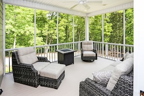 Relax in a serene outdoor space with a forest view, featuring wicker furniture and a ceiling fan.