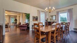 A spacious dining area with a large wooden table and chairs, a chandelier, and a view of the outdoors through large windows. - Private Beach Estate 6B, Group Friendly (Pacific County)