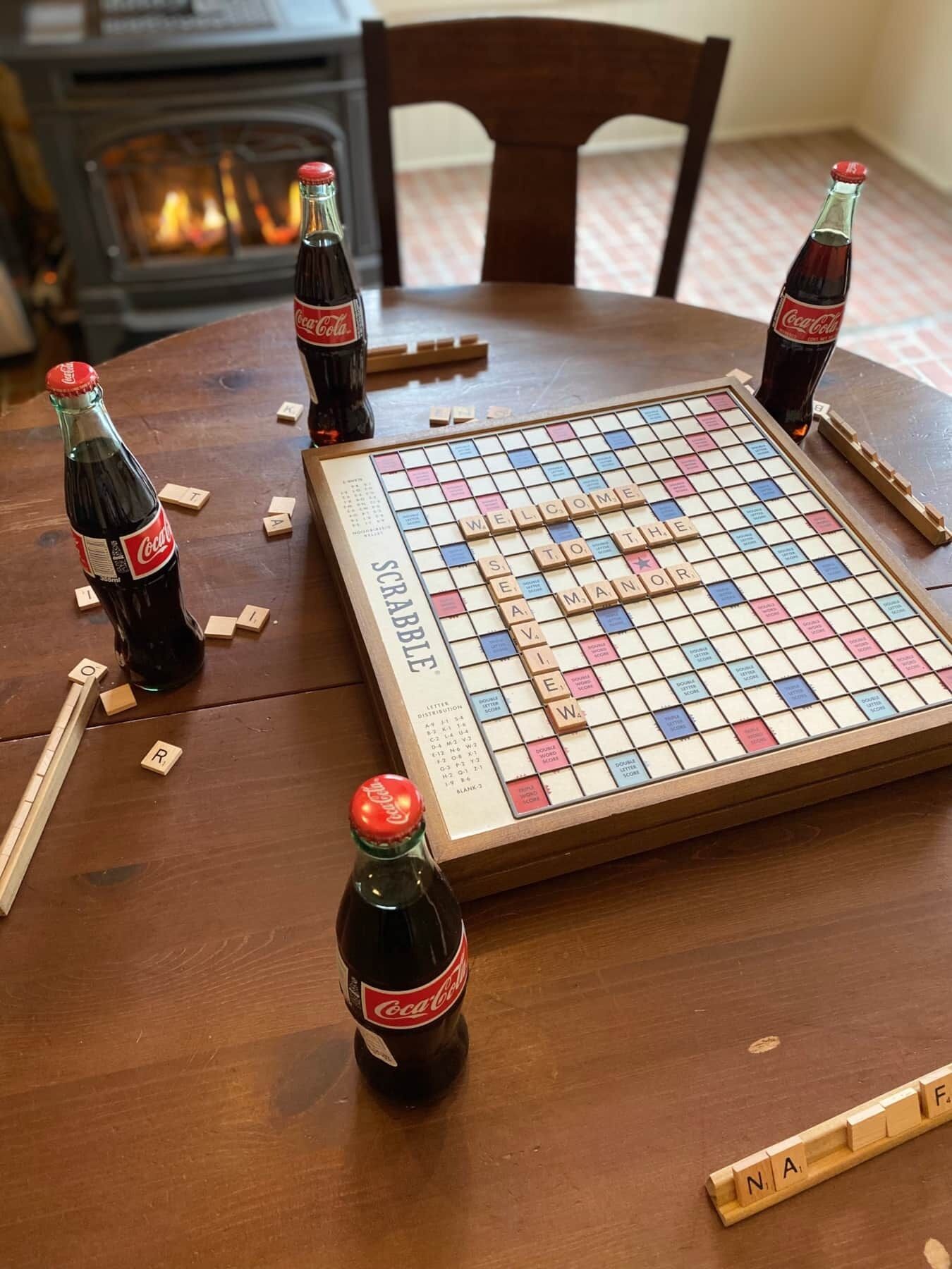 Un juego de Scrabble sobre una mesa de madera con cuatro botellas de Coca-Cola y fichas de letras desperdigadas.
