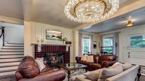 A spacious living room with leather sofas, a fireplace, and a chandelier. - Private Beach Estate 6B, Group Friendly (Pacific County)