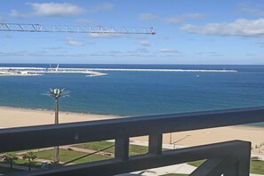 A coastal view from a balcony with a clear sky, a beach, and a distant pier.