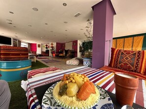 A room with a dining table set with a meal, a colorful striped sofa, and a large window with curtains.