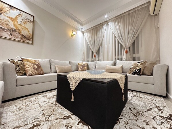 A modern living room with a sectional sofa, a black ottoman, and a marble-patterned rug.