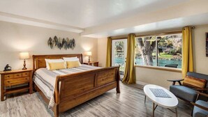 A bedroom with a wooden bed, bedside tables, a small sofa, and a window with curtains. - Pet Friendly Cottage on the River near Downtown! (Bend)