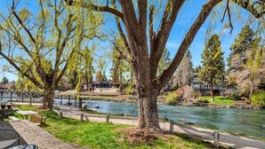 A riverside park with picnic tables, a walking path, and houses in the background. - Pet Friendly Cottage on the River near Downtown! (Bend)