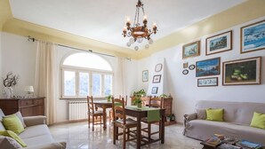 A living room with a dining area, a sofa, a coffee table, and a fireplace. There are several framed pictures on the wall and a chandelier hanging from the ceiling. - Positano: Villa Mamma Rosa with spectacular sea views over the Amalfi Coast (Positano)