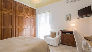 A bedroom with a large bed, a white armchair, a wooden cabinet, a desk, and a television on the wall. - Positano: Villa Mamma Rosa with spectacular sea views over the Amalfi Coast (Positano)