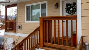 A wooden deck with a railing, a door with a wreath, and a window with blinds. - Immaculate 3 bedroom with hot tub , AC , close to golf course , Whitefish lake , Whitefish Trails! (Whitefish)