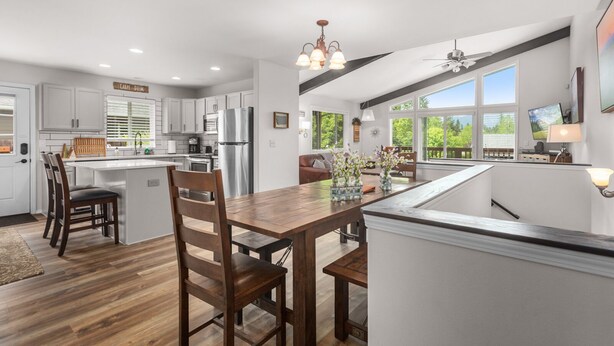 A modern kitchen with white cabinets, a stainless steel refrigerator, and a wooden dining table with chairs. - Immaculate 3 bedroom with hot tub , AC , close to golf course , Whitefish lake , Whitefish Trails! (Whitefish)