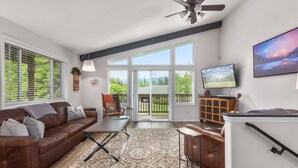 A spacious living room with a brown leather sofa, a patterned rug, and a television on a stand. - Immaculate 3 bedroom with hot tub , AC , close to golf course , Whitefish lake , Whitefish Trails! (Whitefish)