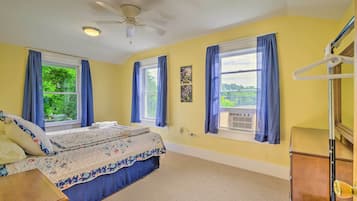 A bedroom with a bed, two windows with curtains, a ceiling fan, and a dresser.