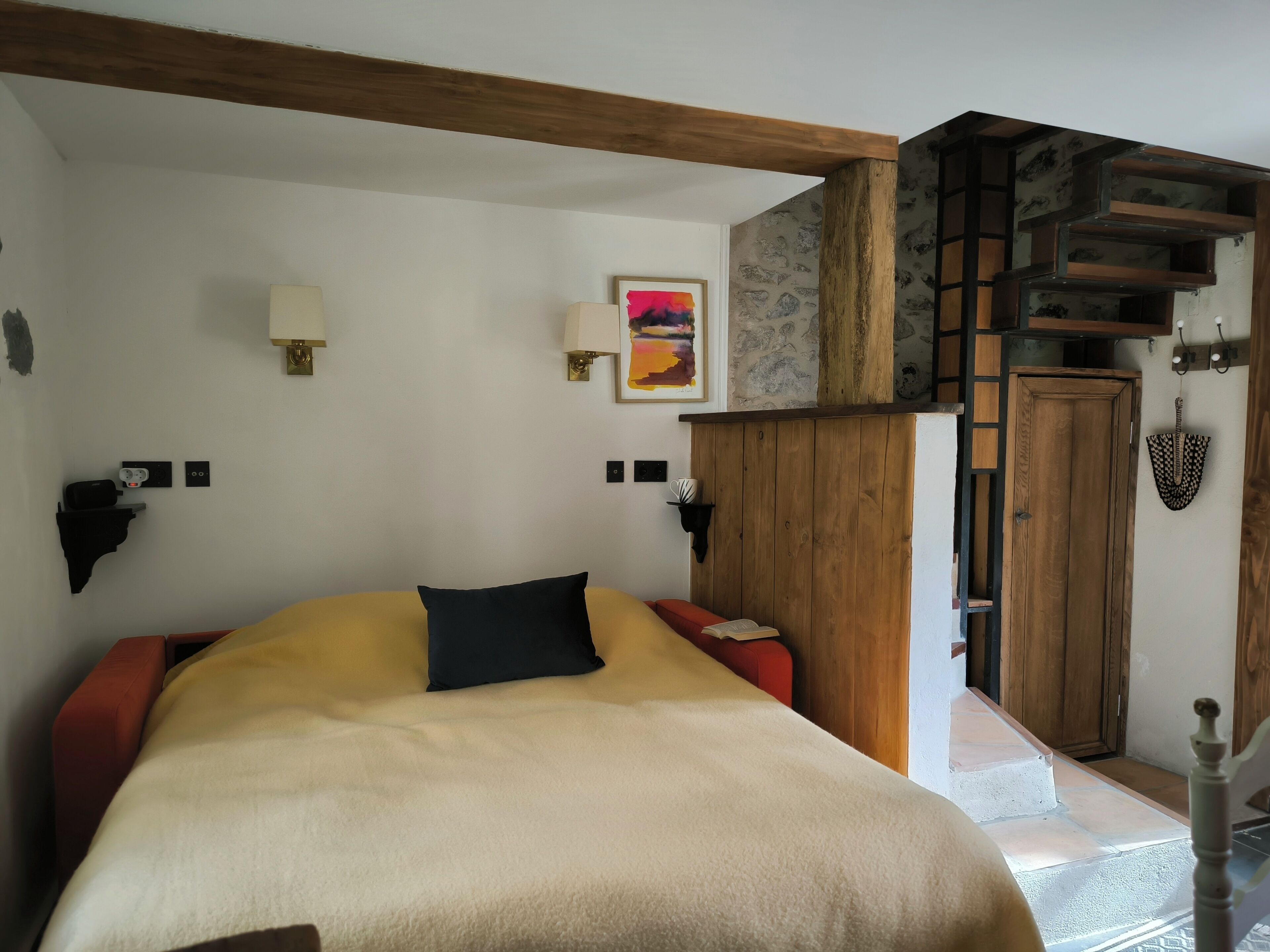 Une chambre à coucher comprenant un lit, une tête de lit en bois, une table de chevet, une lampe et une étagère fixée au mur.