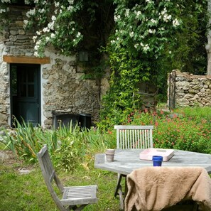 A stone building with a door, a bench, and a table with a cup and a book.