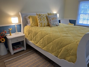 Un lit bien fait, avec une couverture jaune, une lampe de chevet et des coussins décoratifs.
