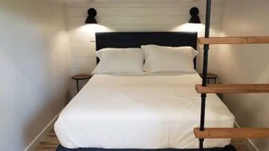 Una cama con cabecera oscura, dos mesitas de noche y una escalera de madera.