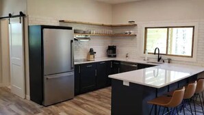 Una cocina moderna con un refrigerador de acero inoxidable, gabinetes negros, una encimera blanca y una zona de bar con taburetes.