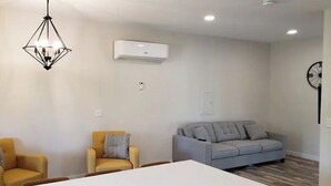 Una sala moderna con un sofá, dos sillones, una mesa de comedor y una lámpara colgante.