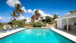 A clear blue pool with lounge chairs, surrounded by palm trees and a white building with a balcony. - Libellule (5 bedrooms) - An idyllic villa with pool, Terres Basses, St. Martin (Terres Basses)
