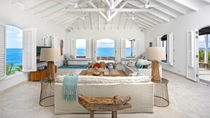 A spacious living room with a high ceiling, large windows with shutters, a central seating area, and a view of the ocean. - Libellule (5 bedrooms) - An idyllic villa with pool, Terres Basses, St. Martin (Terres Basses)
