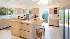 A modern kitchen with a large island, wooden bar stools, and a view of the ocean. - Libellule (5 bedrooms) - An idyllic villa with pool, Terres Basses, St. Martin (Terres Basses)