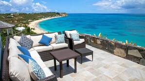 A patio with wicker furniture and a stone wall overlooking a beach. - Libellule (5 bedrooms) - An idyllic villa with pool, Terres Basses, St. Martin (Terres Basses)