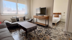 A modern living room with a sofa, a coffee table, a TV on a wooden stand, and a bed with a headboard. - City center apartment perfect for couples in Barcelona (Barcelona)
