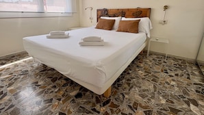 A hotel room with a large bed, a wooden headboard, a window, and a stone-tiled floor. - City center apartment perfect for couples in Barcelona (Barcelona)