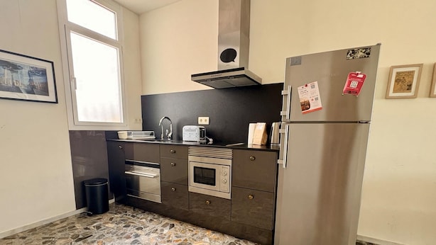A kitchen with a stone-patterned floor, a stainless steel refrigerator, a built-in oven, and a microwave. - City center apartment perfect for couples in Barcelona (Barcelona)