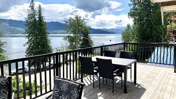 A wooden deck with a table and chairs, overlooking a lake and mountains. - Dancing Waters Lakehouse - Semi Waterfront - Shuswap Vacations and Sledding Accommodation (Anglemont)