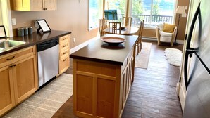 A modern kitchen with wooden cabinets, a dishwasher, and a dining area with a table and chairs. - Dancing Waters Lakehouse - Semi Waterfront - Shuswap Vacations and Sledding Accommodation (Anglemont)