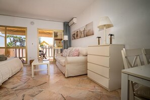 Habitación de hotel con cama, sofá, mesa de comedor, lámpara, cómoda y vistas al exterior.