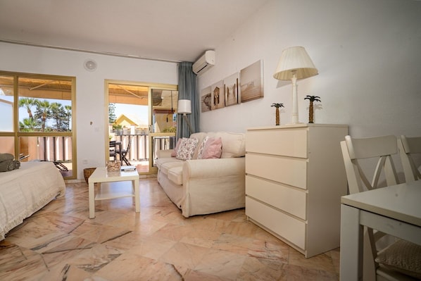 Habitación de hotel con cama, sofá, mesa de comedor, lámpara, cómoda y vistas al exterior.