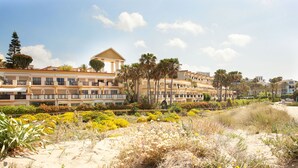 A beachfront hotel with multiple balconies, palm trees, and a sandy beach area.