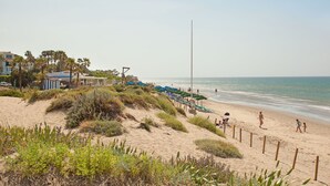 A beach with sand dunes, beach umbrellas, and a few people.