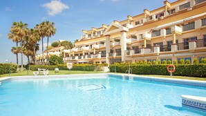 A swimming pool with a clear blue water, surrounded by a building with balconies and palm trees.