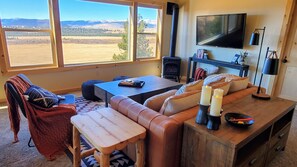 Una sala de estar acogedora con chimenea, un amplio ventanal con vista a las montañas, un sofá confortable y un televisor de pantalla plana.