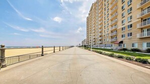 A long, straight pathway leading to a beachfront with a high-rise building on one side. - Oceanfront 3-BR boardwalk condo w indoor pool! (Virginia Beach)