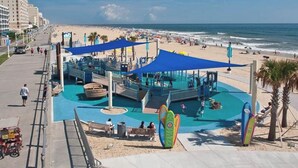 A beachside boardwalk with a water park, palm trees, and a view of the ocean. - Oceanfront 3-BR boardwalk condo w indoor pool! (Virginia Beach)