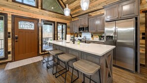 Una cocina moderna con una isla grande, taburetes de bar, electrodomésticos de acero inoxidable y paneles de madera.