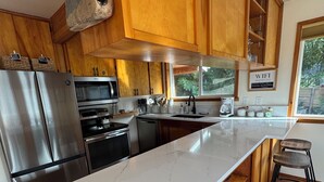 A modern kitchen with wooden cabinets, stainless steel appliances, a marble countertop, and a view of the outdoors. - Riverfront Cabin! BBQ, HOT TUB, FIRE PIT, 4 BEDROOMS (Baring)