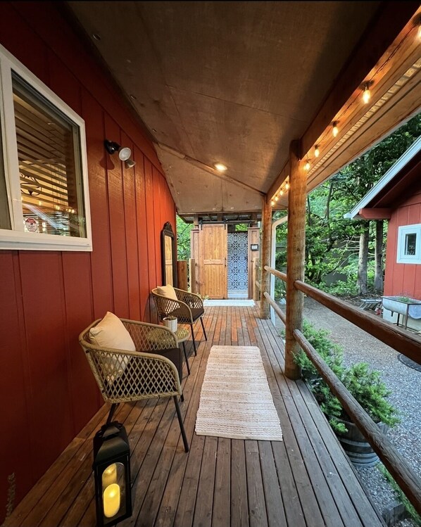 A wooden deck with wicker chairs and a lantern, leading to a door with a patterned glass panel. - Riverfront Cabin! BBQ, HOT TUB, FIRE PIT, 4 BEDROOMS (Baring)